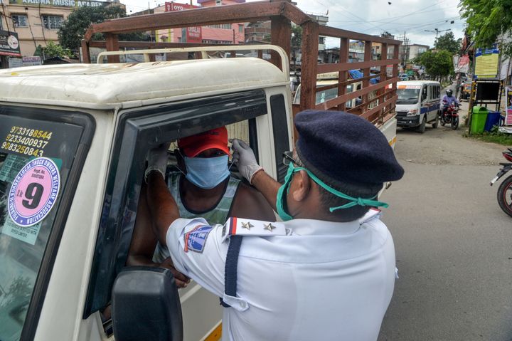 A police personnel adjusts a facemask on a motorist near a contained area after some residents allegedly tested positive for the COVID-19 coronavirus in Siliguri on June 17, 2020.