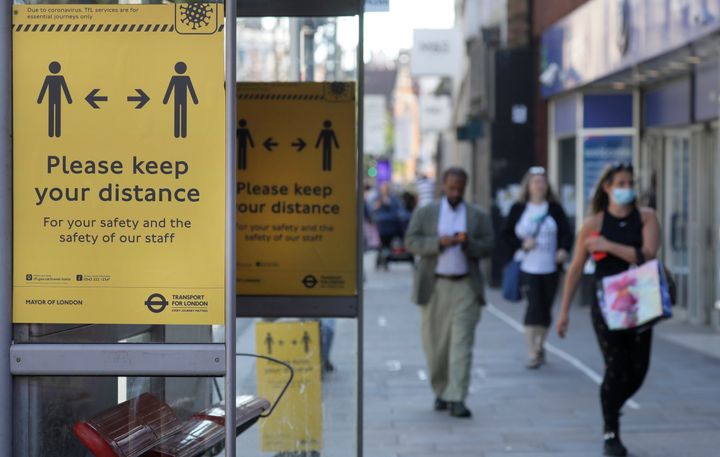 Signs advise people to social distance on a bus stop along a high street, in London