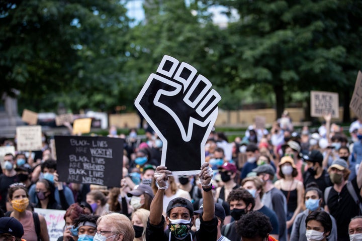 A protester wearing a mask holds a large Black power raised fist in the middle of a crowd that gathered at Columbus Circle on June 14, 2020, in New York City.