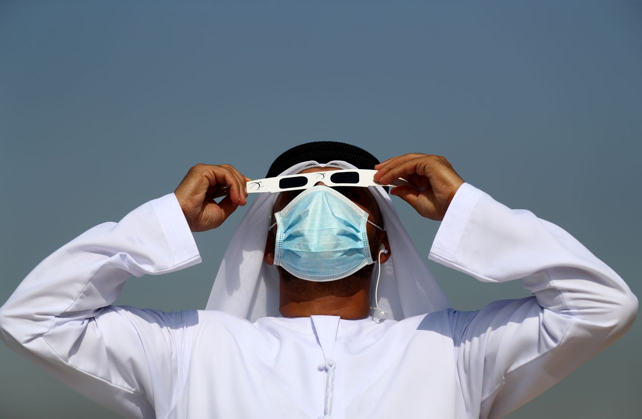 Ένας άντρας φοράει μάσκα προσώπου καθώς παρατηρεί τη μερική ηλιακή έκλειψη μέσα από γυαλιά ηλίου την Κυριακή στο Al Thuraya Astronomy Center στο Ντουμπάι στα Ηνωμένα Αραβικά Εμιράτα.