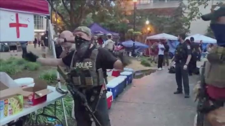 A police officer, wearing a tactical vest, gestures for people to step back after the shooting.