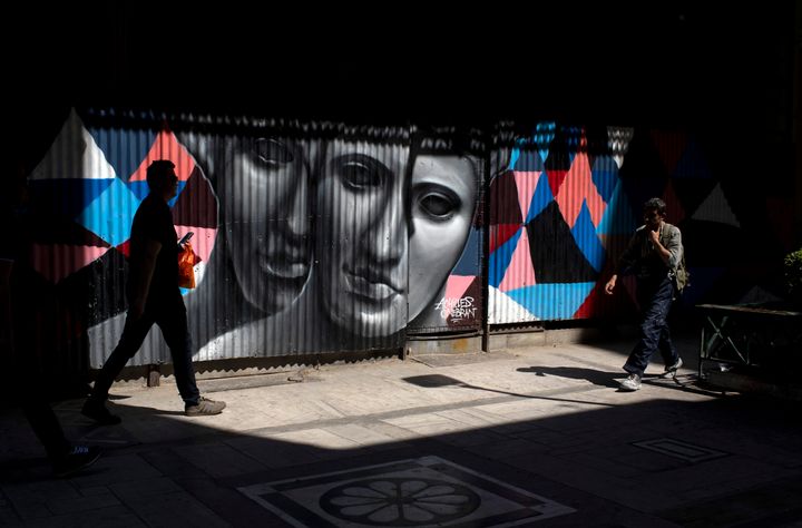 Pedestrian walk past a graffiti made by street artist Achilles in Athens, on Monday, June 3, 2019. (AP Photo/Petros Giannakouris)
