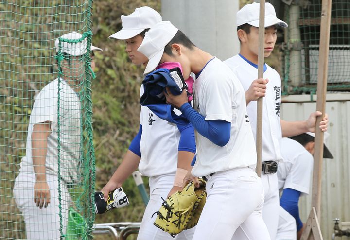 全国高校野球選手権大会の中止を伝えられ、タオルで顔を覆いグラウンドを出る大分・明豊の選手（中央）