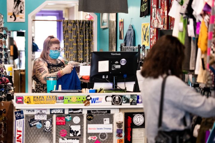 A worker wears a face mask at Sid and Nancy thrift and consignment store in Columbia, South Carolina, as a shopper browses a rack of clothes on April 23, 2020.
