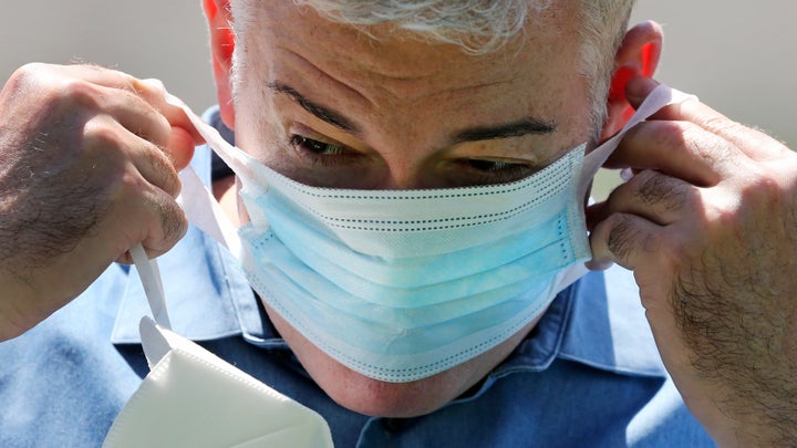 Williams stretches the thin cloth band of a surgical mask, provided by FEMA, over his face.