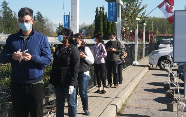 People wear face masks and practice physical distancing while waiting to enter a garden centre in Toronto,...