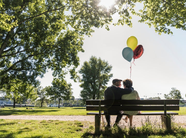 Happy senior couple with balloons sitting on bench in a park