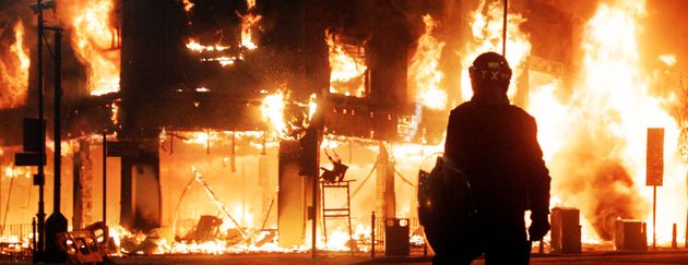 Riot police look on as fire rages through a building in Tottenham, north London, as trouble flared after members of the community took to the streets last night to demand 