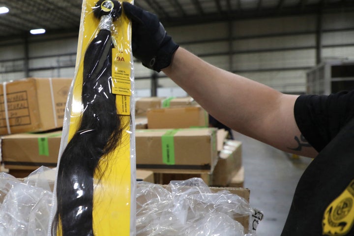 In this June 29, 2020, photo provided by U.S. Customs and Border Protection, a field operations officer inspects a suspect hair accessory at a centralized exam station in Newark, N.J. On Wednesday, July 1, 2020, U.S. Customs and Border Protection detained a shipment of weaves believed to be made in a Chinese detention camp. The shipment is suspected to be human hair. Some information on the package was blurred by the source. (U.S. Customs and Border Protection via AP)