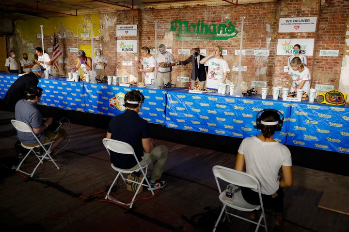 Competitors separated by translucent panels eat in the women's division of the Nathan's Famous July Fourth hot dog eating contest during the coronavirus pandemic, Saturday, July 4, 2020, in the Brooklyn borough of New York. (AP Photo/John Minchillo)