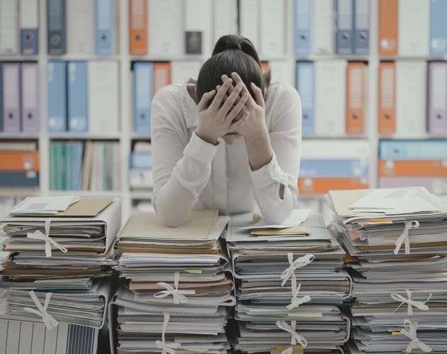 Frustrated you office worker leaning on piles of paperwork, she is overloaded with work and stressed