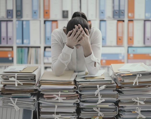 Frustrated you office worker leaning on piles of paperwork, she is overloaded with work and stressed