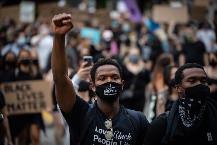 A man wearing a face mask that says "I Can't Breathe" and "Black Lives Matter" raises his fist while marching with thousands of others to mark Juneteenth in Vancouver on June 19, 2020. 