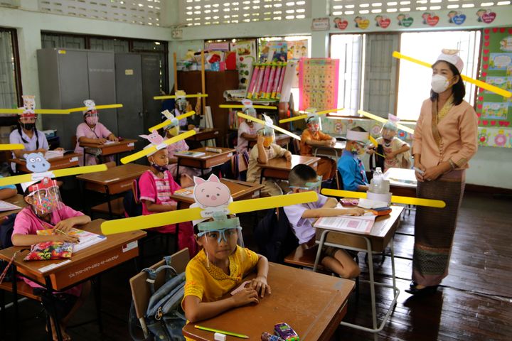 A teacher and students wearing hats designed to help them practice social distancing at a school in Thailand. 