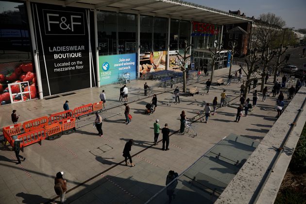 People observe social distancing as they queue up to shop outside a branch of the Tesco supermarket chain in west London, Friday, April 10.