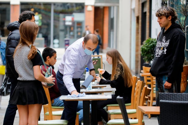 A waiter wipes down a table before seating customers at a restaurant in central London.
