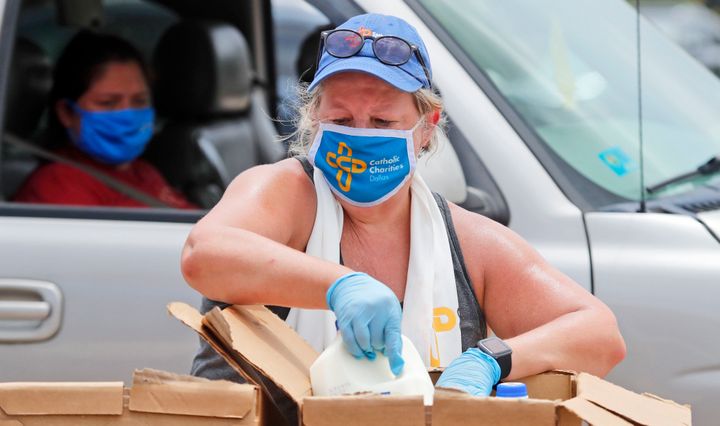 Wearing a mask amid concerns of the spread of COVID-19, volunteer Karen Cooperstein handles chilled milk for the pubic during a drive through food pantry distribution by Catholic Charities in Dallas, Thursday, July 2, 2020. 