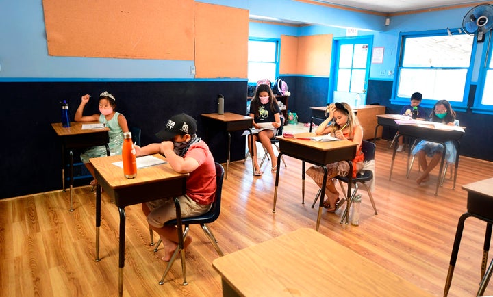 Children in an elementary school class wear masks and sit as desks spaced apart during summer school at Happy Day School in M