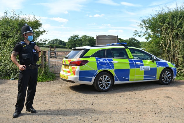 A police officer wearing a face mask at Rook Row Farm in Mathon, near Malvern, Herefordshire, where there have been 73 positive cases of coronavirus confirmed.