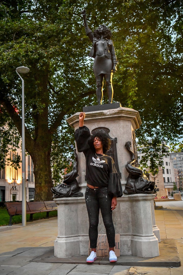 Jen Reid poses in front of her black resin and steel statue titled A Surge of Power (Jen Reid) 2020, by Marc Quinn, where it is installed on the vacant Edward Colston plinth in Bristol city centre.