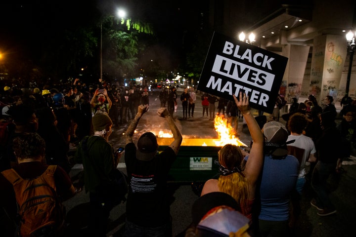 A waste receptacle's contents are in flames as protesters gather in downtown Portland, Ore. on July 10, 2020. The mayor of Portland said late Sunday the U.S. Marshals Service are investigating the injury of a protester who was hospitalized in critical condition over the weekend after being hit in the head by an impact weapon fired by a federal law enforcement officer.