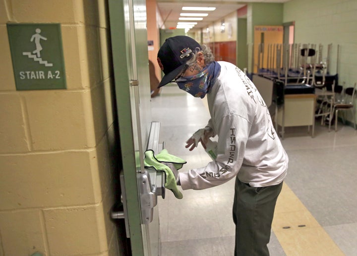 A custodian wipes down a hallway doorway at the Mildred Avenue K-8 School building in Boston ahead of the school reopening last week. School systems are taking many measure to keep students safe during the pandemic, including placing social distancing markers on the floors and increasing hand sanitizer stations.