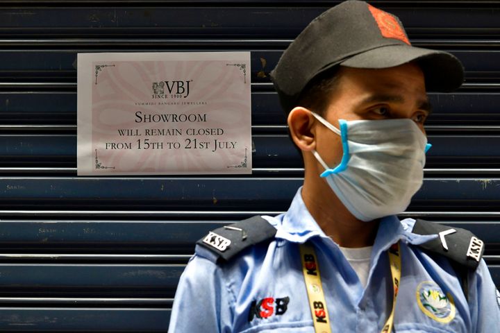 A security guard stands outside a closed jewelry store next to a sign informing customers of a weeklong closure as Bengaluru undergoes a lockdown to contain the surge of coronavirus cases, July 14, 2020.