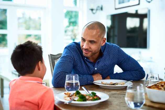 Mature man leaning forward towards boy, food on dining room table, family meal time, conversation, bonding