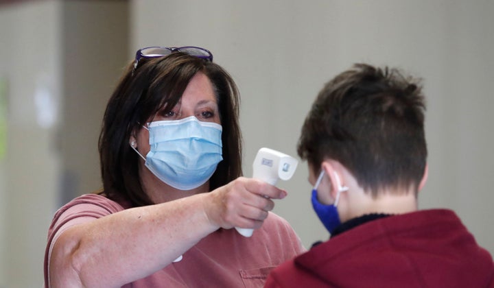 Amid concerns of the spread of COVID-19, science teacher Ann Darby uses a thermometer on Tuesday to check a student's temperature prior to a summer science, technology, engineering and mathematics (STEM) camp at Wylie High School in Wylie, Texas. Schools and educators across the U.S. find themselves in the middle of an increasingly politicized debate over how best to reopen schools later this year.