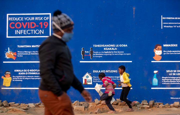 People walk past a Covid-19 advert promoting the use of face masks, washing of hands, use of sanitiser and social distancing in the township of Soweto outside of Johannesburg.