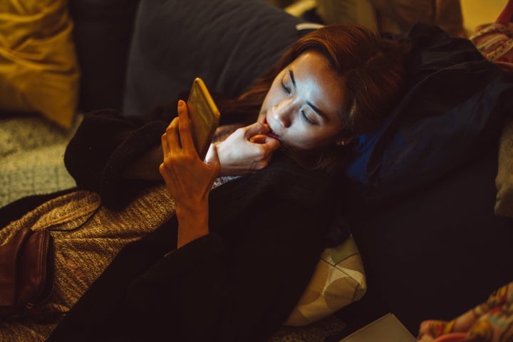 Pretty young lady biting her fingernail while using smartphone at home in the night