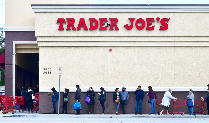 A woman wearing a facemask pushes her cart to the back of the line as people line up before the opening of a Trader Joe's sto