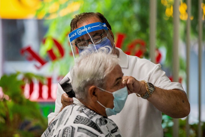 Joaquim Correia, du College Barber Shop, coupe les cheveux d'un client alors que la phase 2 d'assouplissement des mesures liées à la COVID-19 commence à Toronto, en Ontario, le 24 juin 2020.