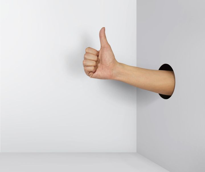 A hand gives a thumb's up out of a hole in the wall.