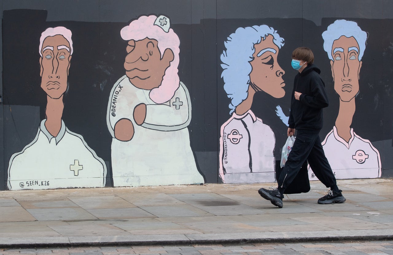 A man wearing a protective face mask passes a mural showing BAME medical and transport workers, in Waterloo, London.