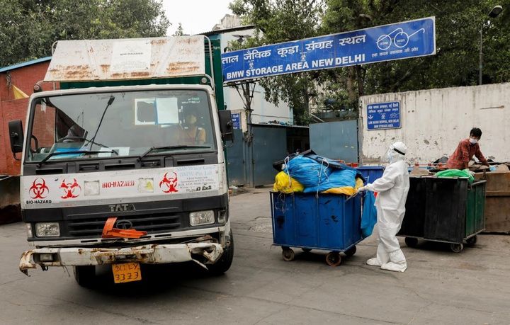 A man wearing personal protective equipment pushes a trolley containing medical waste bags to a Bio-Medical Waste storage area.