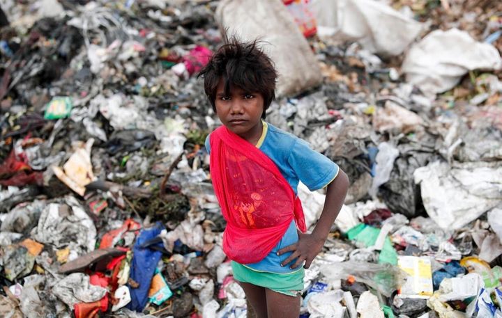 A young waste collector waits for a truck to offload rubbish onto a landfill site.