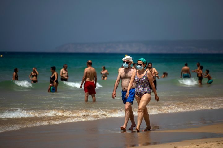 A couple wearing face masks walk along the shore in a beach in Cadiz, south of Spain, on Tuesday, July 21, 2020. (AP Photo/Emilio Morenatti)