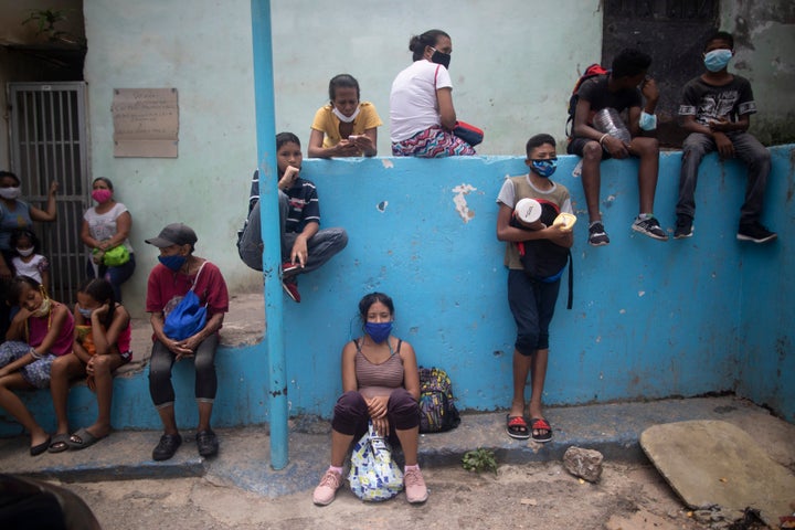 Residents wearing protective face masks wait outside a soup kitchen to receive pack-and-go lunches in the Petare neighborhood of Caracas, Venezuela, Wednesday, July 15, 2020, amid the new coronavirus pandemic. 