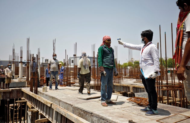 A health worker uses an infrared thermometer to measure the temperature of a labourer at the construction...