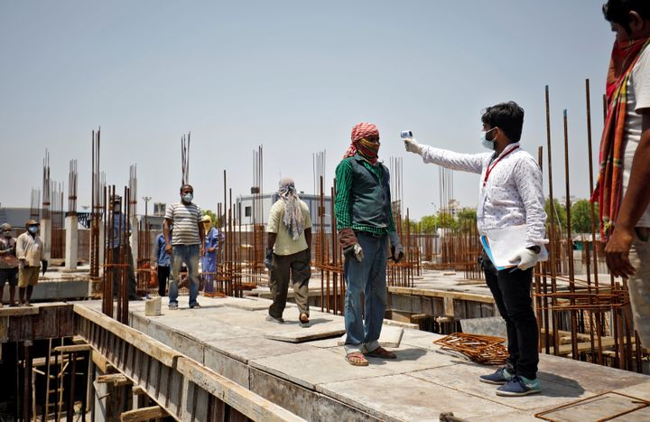 A health worker uses an infrared thermometer to measure the temperature of a labourer at the construction site of a residential building in Ahmedabad, Gujarat, April 30, 2020. 