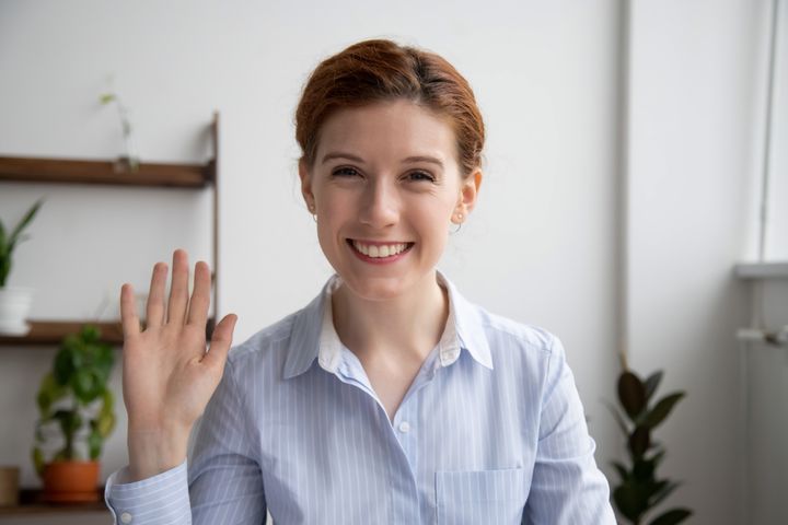 Head shot portrait of attractive smiling businesswoman waving hand, looking at camera, making video call with webcam, greeting, business coach recording video for vlog, saying hello