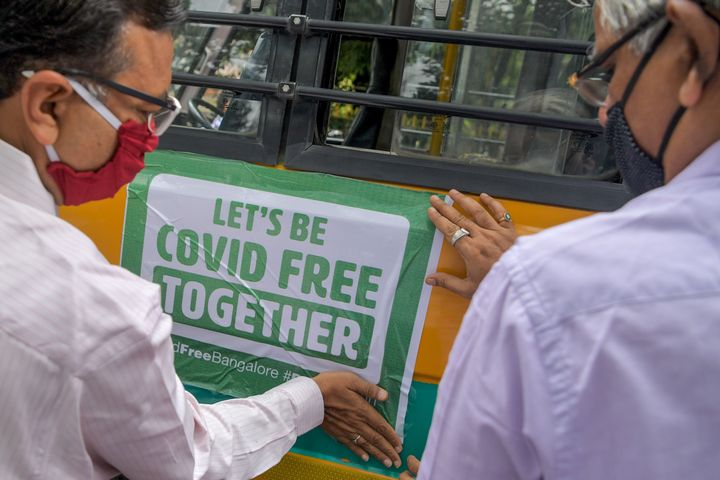 Municipality officials stick a banner on a vehicle transporting lab workers from Primary Health Centres (PHC) to conduct tests using Rapid Antigen test kits in containment zones in Bangalore on July 17, 2020