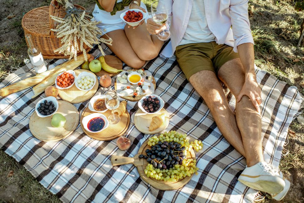 Couple having romantic breakfast outdoors, close-up view on the picnic blanket with lots of tasty food
