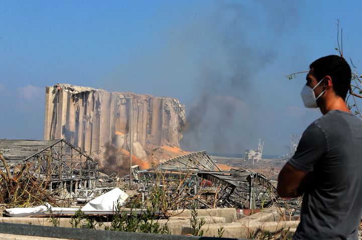 A man wearing a protective mask against the coronavirus stands across the road from the damaged grain silos of Beirut's harbour August 5, 2020, one day after a powerful twin explosion tore through Lebanon's capital, resulting from the ignition of a huge depot of ammonium nitrate at the city's main port.