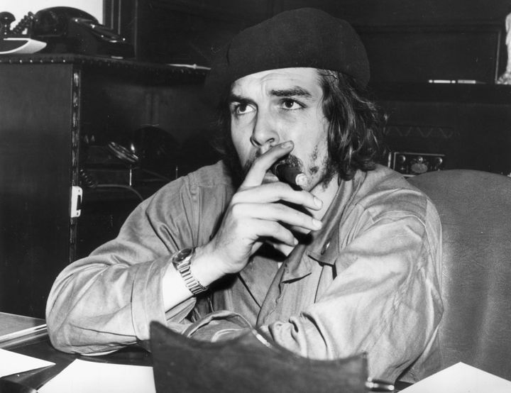 1959: Argentine-born Cuban revolutionary leader and economic advisor Ernesto 'Che' Guevara (1928 - 1967) sits at a desk and smokes a cigar, wearing military fatigues and a beret. After aiding Fidel Castro's successful overthrow of the Batista regime, Guevara served as economic advisor in Castro's administration. (Photo by Hulton Archive/Getty Images)