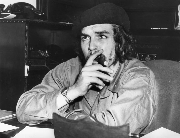 1959: Argentine-born Cuban revolutionary leader and economic advisor Ernesto 'Che' Guevara (1928 - 1967) sits at a desk and smokes a cigar, wearing military fatigues and a beret. After aiding Fidel Castro's successful overthrow of the Batista regime, Guevara served as economic advisor in Castro's administration. (Photo by Hulton Archive/Getty Images)