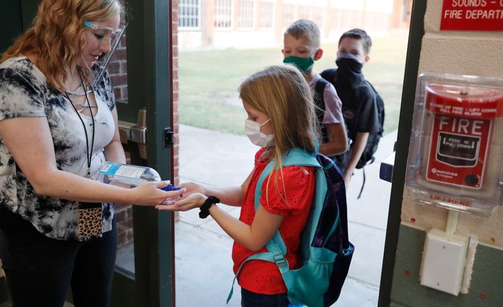 Wearing masks to prevent the spread of COVID-19, elementary school students use hand sanitizer before entering their classroom in Godley, Texas, on Wednesday. Schools across the country have grappled with the issue of whether to resume in-person classes or conduct them online amid the pandemic.