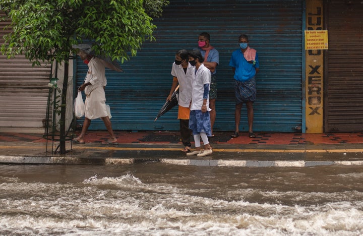 Two medical workers wearing masks as a precaution against the coronavirus assess the water level as they try to cross a flooded street during heavy rainfall in Kochi,, Aug. 7, 2020. 