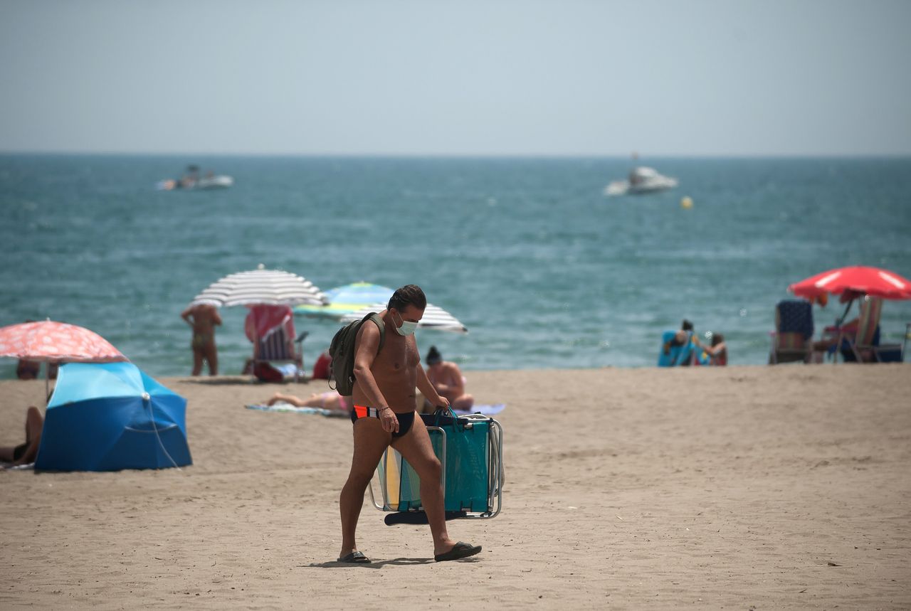 A man wearing a face mask carrying chairs at Rincon Sol beach of Torremolinos in Malaga during a hot summer day.